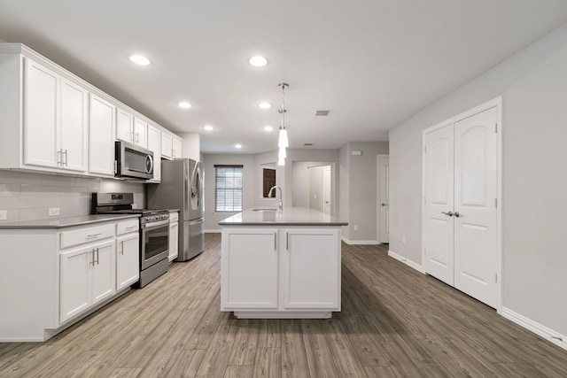 kitchen featuring appliances with stainless steel finishes, pendant lighting, white cabinets, and an island with sink