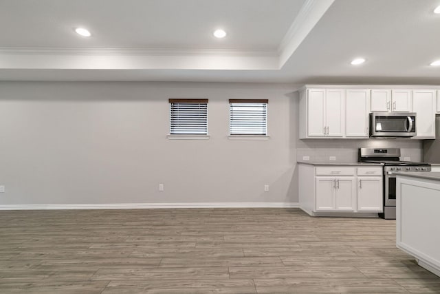 kitchen with white cabinets, appliances with stainless steel finishes, ornamental molding, light wood-type flooring, and a tray ceiling