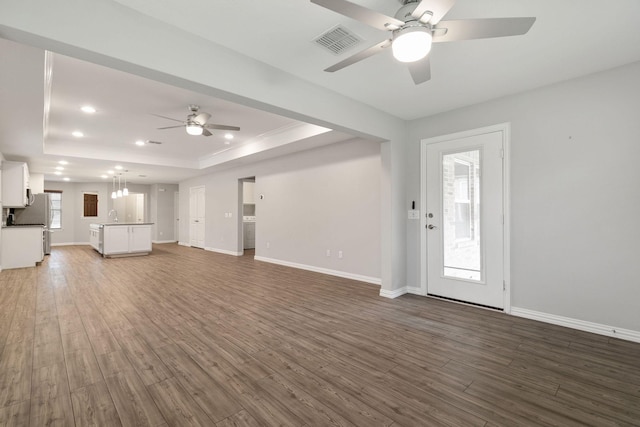 unfurnished living room featuring dark hardwood / wood-style floors, ceiling fan, a raised ceiling, and sink