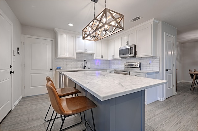 kitchen with a kitchen island, stainless steel appliances, pendant lighting, white cabinetry, and light hardwood / wood-style flooring