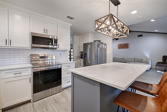 kitchen with white cabinets, pendant lighting, a kitchen bar, appliances with stainless steel finishes, and light hardwood / wood-style floors