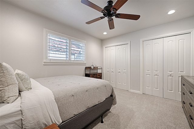 bedroom featuring ceiling fan, multiple closets, and light colored carpet