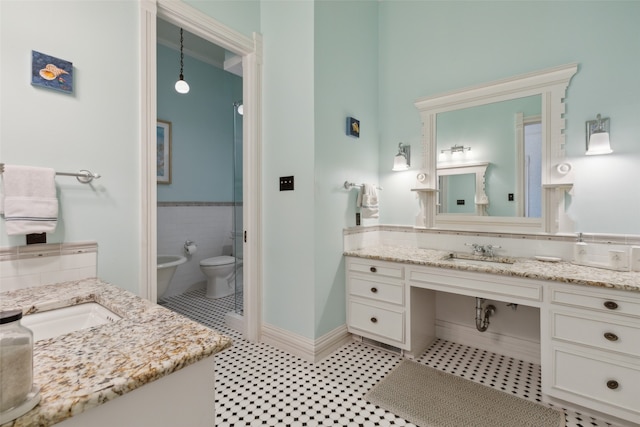 bathroom with toilet, a bidet, vanity, and tile walls