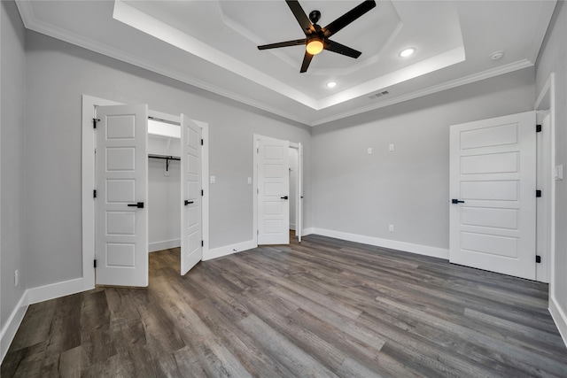 unfurnished bedroom with ornamental molding, ceiling fan, dark hardwood / wood-style floors, a tray ceiling, and a walk in closet