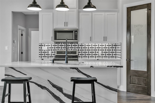 kitchen featuring stainless steel appliances, light stone counters, hanging light fixtures, white cabinets, and dark hardwood / wood-style flooring