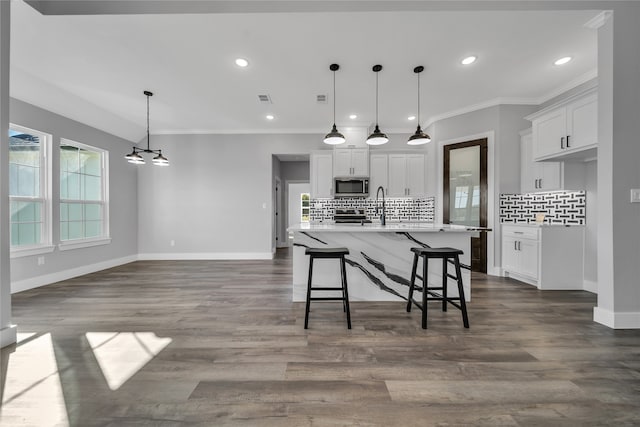 kitchen with white cabinetry, decorative backsplash, decorative light fixtures, and an island with sink