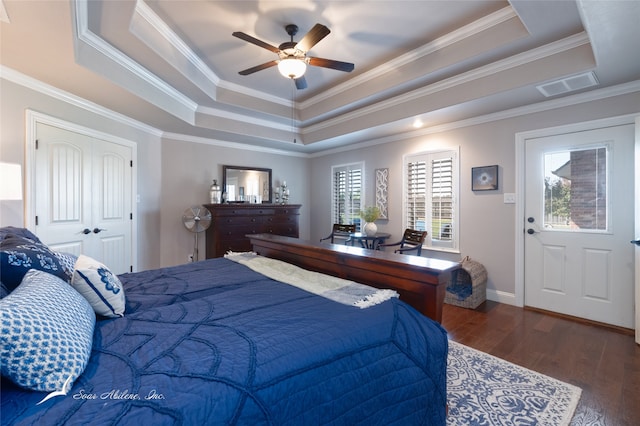 bedroom with ceiling fan, a tray ceiling, crown molding, and dark wood-type flooring