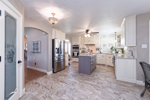 kitchen with a kitchen island, light stone counters, backsplash, appliances with stainless steel finishes, and white cabinetry