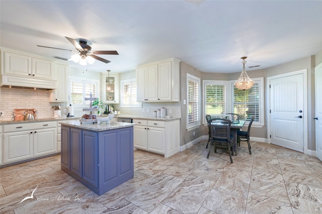 kitchen featuring a kitchen island, light stone counters, decorative backsplash, white cabinets, and hanging light fixtures