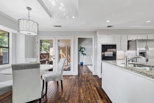 kitchen with light stone countertops, stainless steel fridge, black oven, white cabinetry, and hanging light fixtures