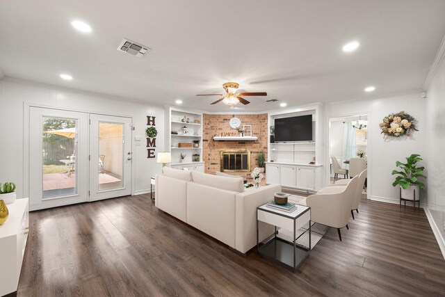 living room with crown molding, dark hardwood / wood-style floors, built in features, a fireplace, and ceiling fan with notable chandelier