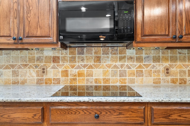 kitchen featuring decorative backsplash, light stone counters, and black appliances