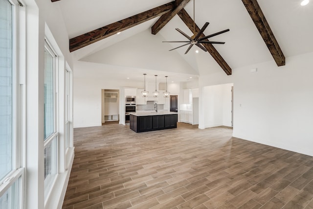 unfurnished living room featuring beamed ceiling, ceiling fan, sink, and wood-type flooring