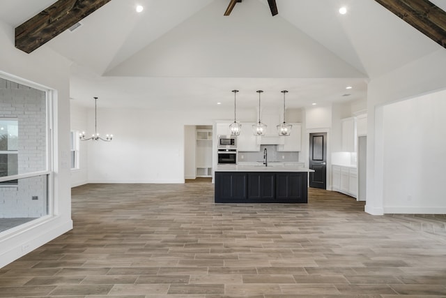 kitchen featuring light wood-type flooring, a kitchen island with sink, hanging light fixtures, and white cabinetry