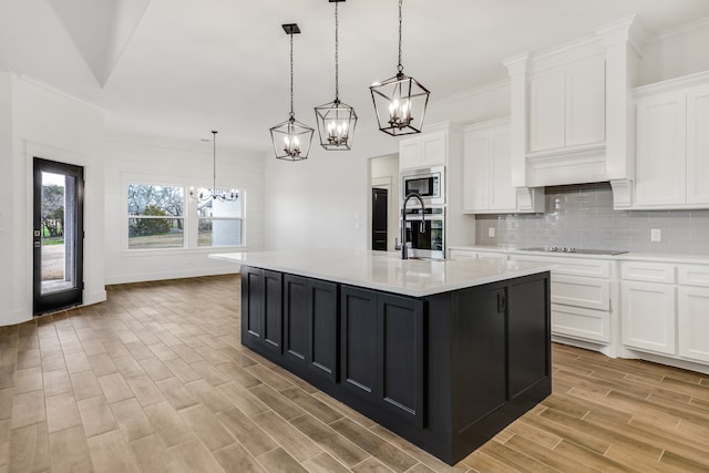 kitchen featuring an island with sink, decorative light fixtures, appliances with stainless steel finishes, and white cabinetry