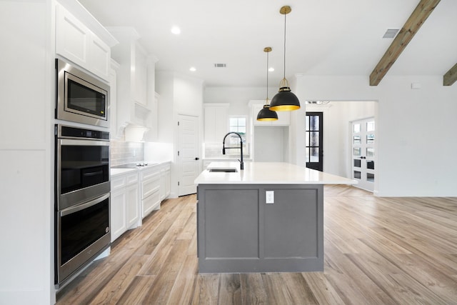 kitchen featuring a kitchen island with sink, sink, decorative backsplash, white cabinets, and appliances with stainless steel finishes