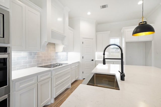 kitchen featuring pendant lighting, light hardwood / wood-style flooring, sink, black electric stovetop, and white cabinetry