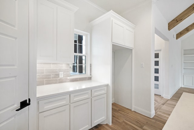 kitchen featuring light hardwood / wood-style floors, lofted ceiling with beams, tasteful backsplash, crown molding, and white cabinetry