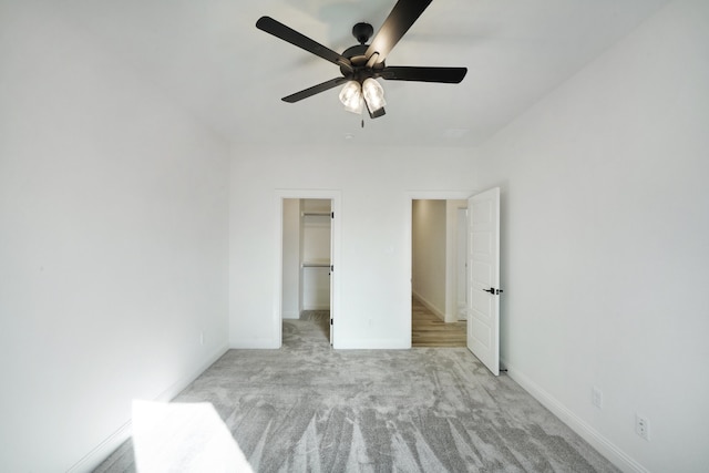 unfurnished bedroom with a closet, light carpet, a walk in closet, and ceiling fan