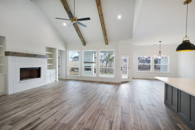 unfurnished living room featuring beam ceiling, high vaulted ceiling, a fireplace, ceiling fan with notable chandelier, and light hardwood / wood-style floors