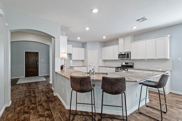 kitchen featuring kitchen peninsula, appliances with stainless steel finishes, white cabinets, light stone counters, and a breakfast bar