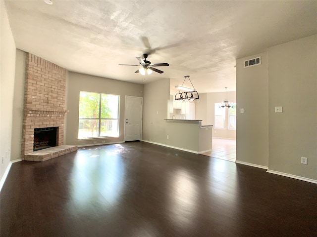 unfurnished living room with ceiling fan with notable chandelier, a fireplace, and dark hardwood / wood-style floors