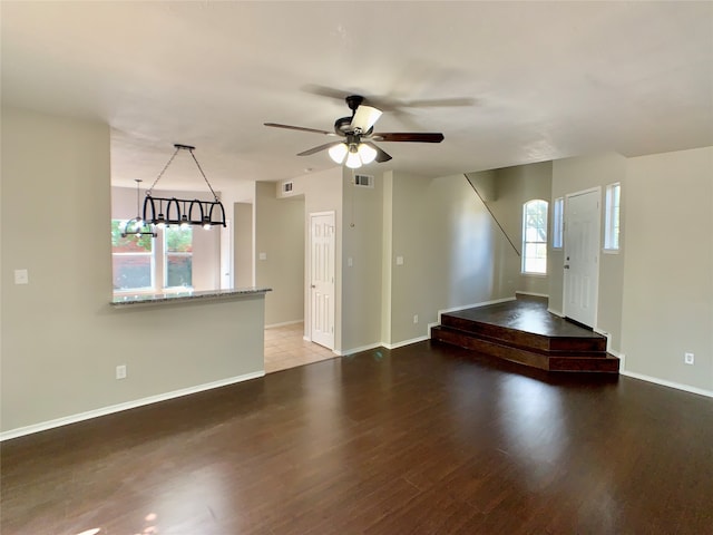 interior space with ceiling fan with notable chandelier, dark wood-type flooring, and a wealth of natural light