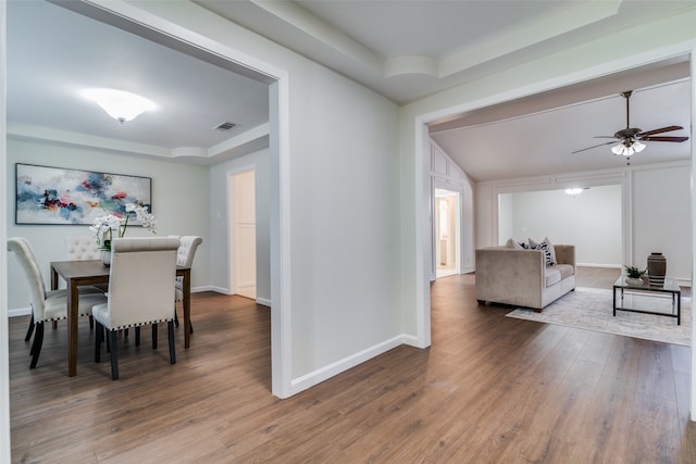 dining area with wood-type flooring, a tray ceiling, and ceiling fan