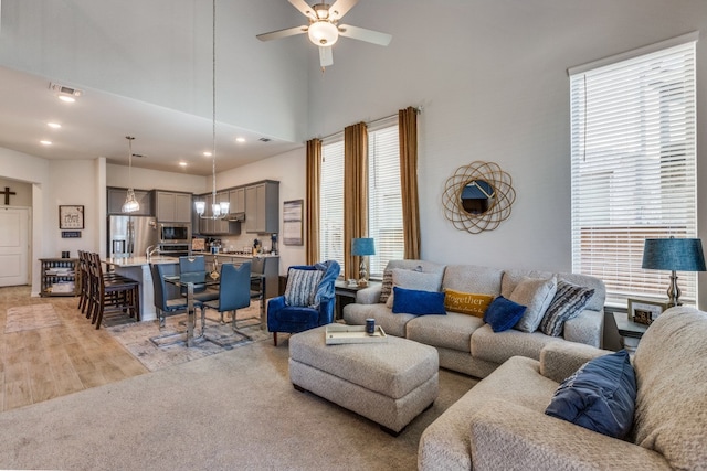 living room featuring ceiling fan, a towering ceiling, and light colored carpet