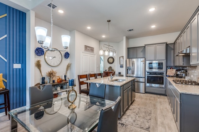 kitchen with light stone counters, decorative light fixtures, stainless steel appliances, and light hardwood / wood-style floors