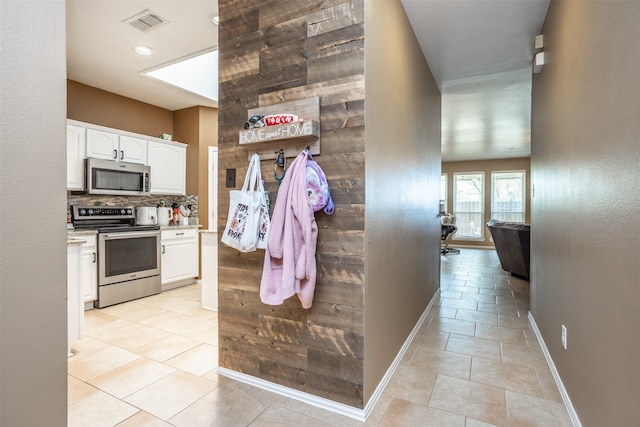 kitchen with appliances with stainless steel finishes, backsplash, light tile patterned floors, and white cabinetry