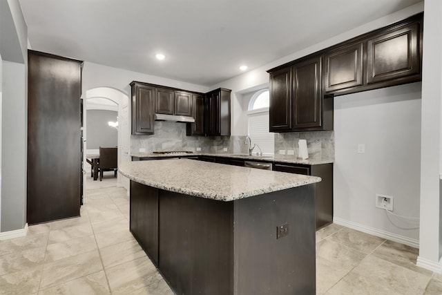 kitchen with a kitchen island, stainless steel appliances, sink, light stone counters, and tasteful backsplash