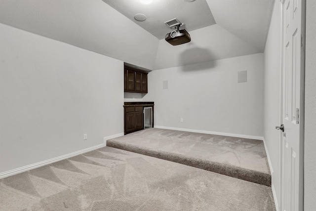 unfurnished living room featuring light carpet, bar, and vaulted ceiling