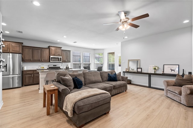 living room featuring sink, light hardwood / wood-style flooring, and ceiling fan