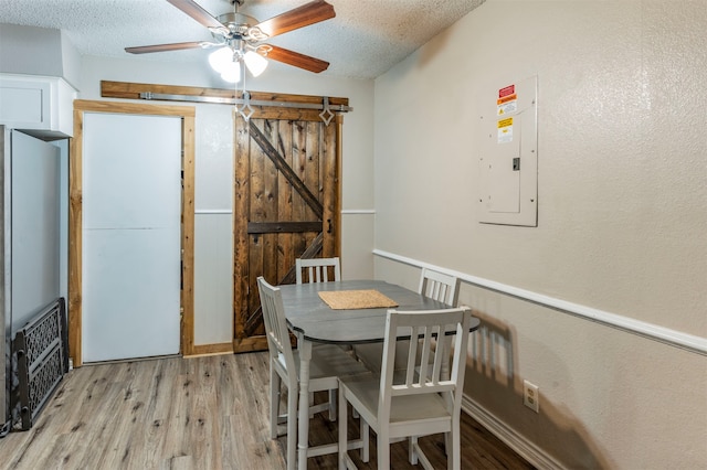 dining area featuring electric panel, light hardwood / wood-style floors, a barn door, and a textured ceiling