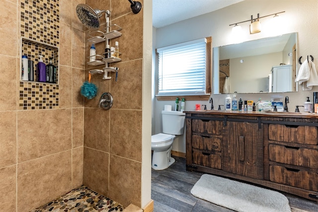 bathroom with toilet, tiled shower, vanity, and wood-type flooring