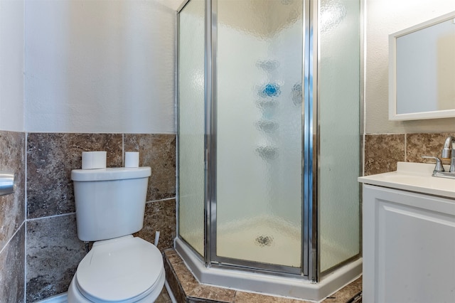 bathroom with vanity, tile walls, a shower with shower door, and toilet