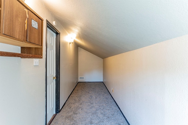 corridor featuring a textured ceiling, vaulted ceiling, and light colored carpet