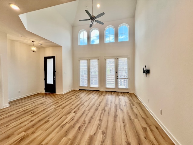 unfurnished living room featuring french doors, ceiling fan with notable chandelier, light wood-type flooring, and high vaulted ceiling