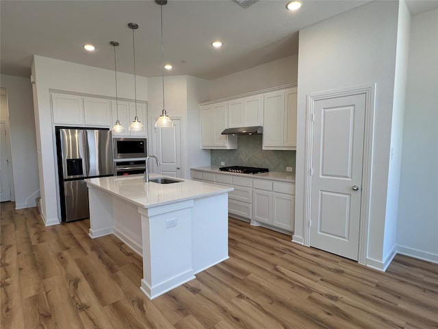 kitchen with a kitchen island with sink, stainless steel appliances, tasteful backsplash, sink, and white cabinetry