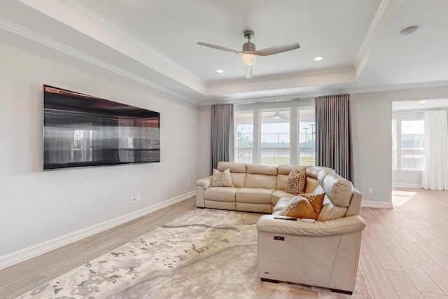 living room with a raised ceiling, light wood-type flooring, plenty of natural light, and ornamental molding