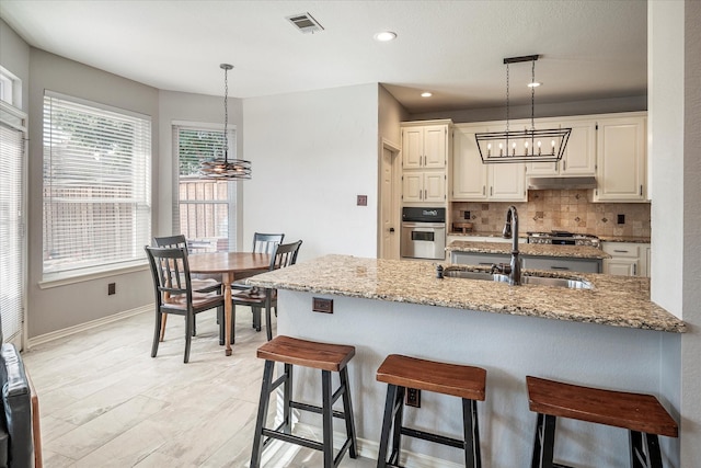 kitchen featuring tasteful backsplash, light stone counters, stainless steel oven, sink, and hanging light fixtures