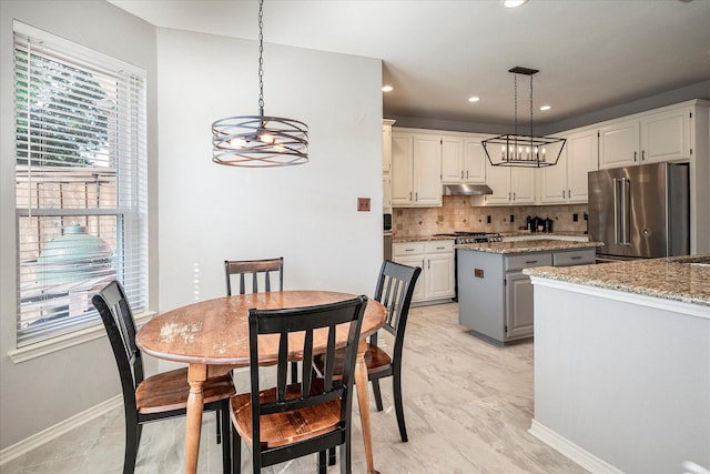 kitchen with appliances with stainless steel finishes, decorative light fixtures, a kitchen island, and light stone counters