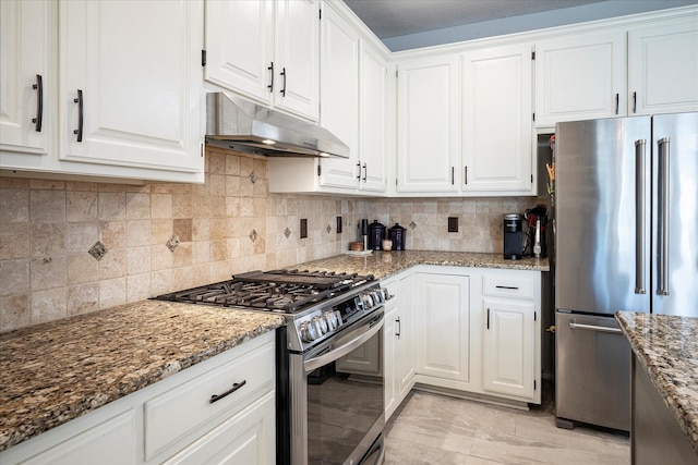 kitchen featuring dark stone counters, decorative backsplash, light tile patterned floors, appliances with stainless steel finishes, and white cabinetry