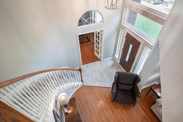 foyer entrance with wood-type flooring, a towering ceiling, and an inviting chandelier