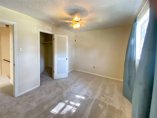 unfurnished bedroom featuring ceiling fan, light colored carpet, a textured ceiling, and a closet