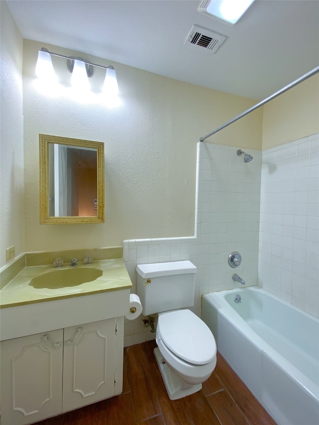 full bathroom featuring toilet, hardwood / wood-style floors, tile walls, tiled shower / bath, and vanity