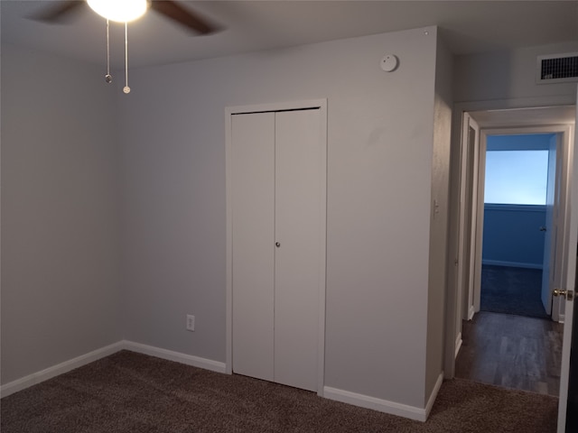 unfurnished bedroom with ceiling fan, a closet, and dark colored carpet