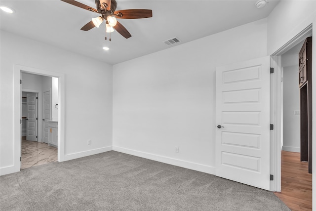 unfurnished bedroom with light colored carpet, ensuite bathroom, and ceiling fan