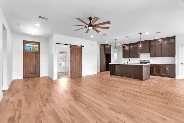 kitchen with decorative light fixtures, a center island with sink, light wood-type flooring, a barn door, and decorative backsplash